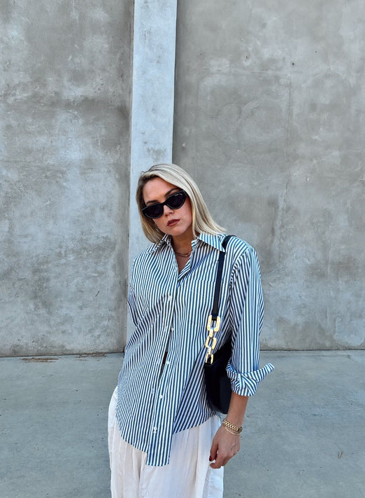 Woman wearing a green and white striped shirt with white pants against a gray wall.