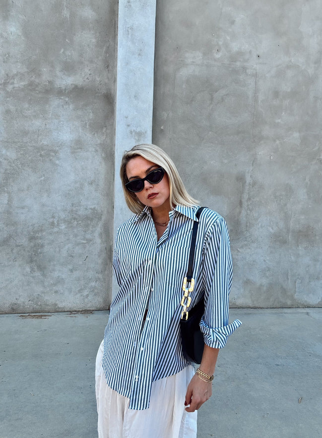 Woman wearing a green and white striped shirt with white pants against a gray wall.