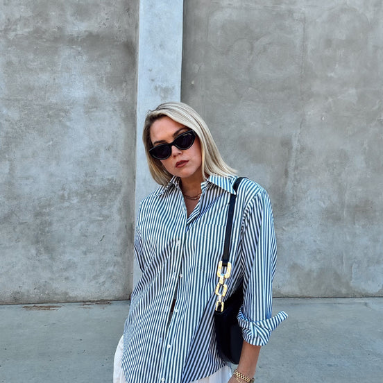 Woman wearing a green and white striped shirt with white pants against a gray wall.