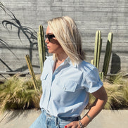 Person wearing a light green shirt and jeans standing near a pool with cacti in the background