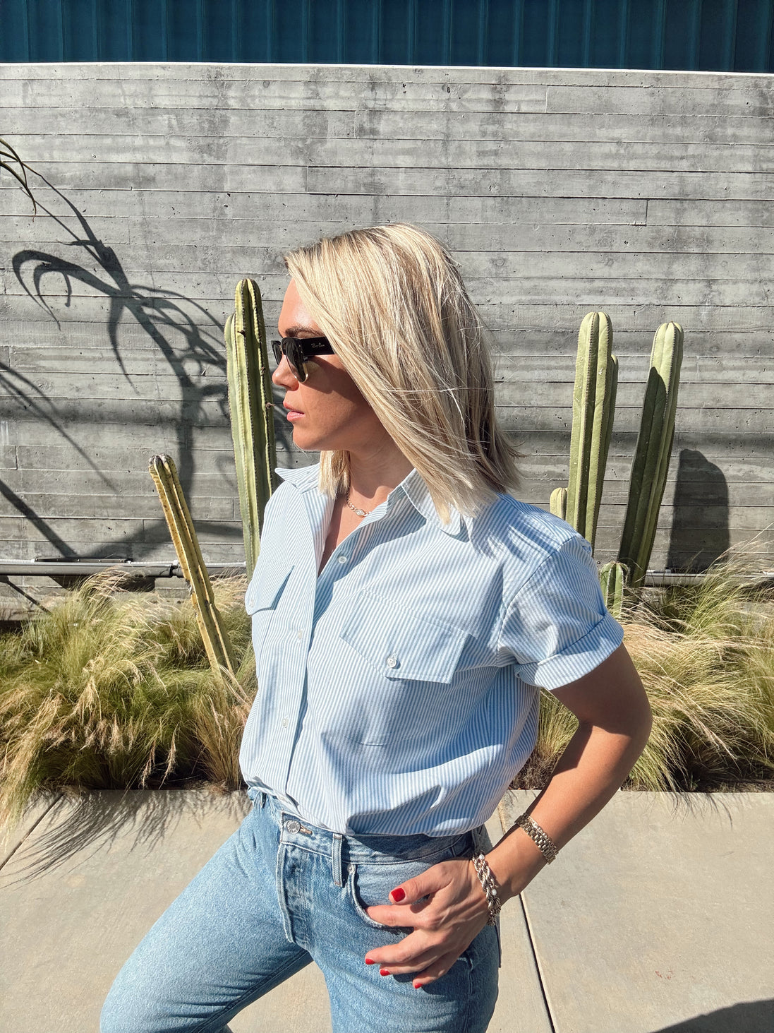 Person wearing a light green shirt and jeans standing near a pool with cacti in the background