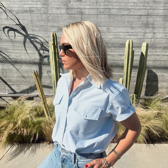 Person wearing a light green shirt and jeans standing near a pool with cacti in the background