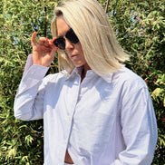 Person wearing a light purple striped shirt with sunglasses, standing against a green leafy background